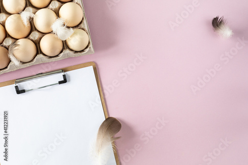 A box of organic fresh chicken eggs and slipboard on pink background. Eco-friendly egg production. photo