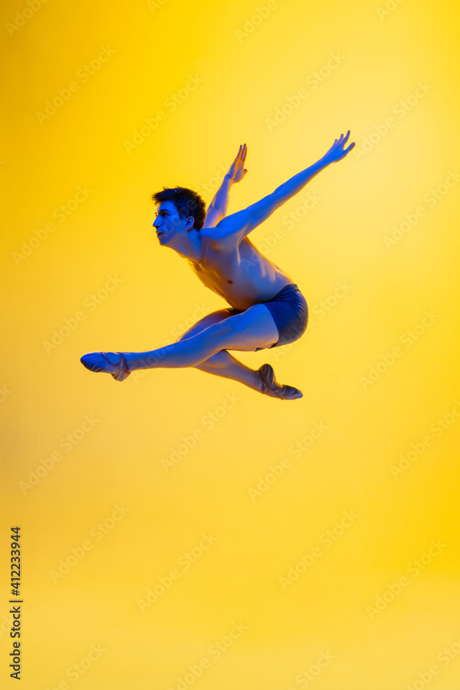 Bird's freedom. Young and graceful ballet dancer on yellow studio background in neon light. Art, motion, action, flexibility, inspiration concept. Flexible caucasian ballet dancer, moves in glow.
