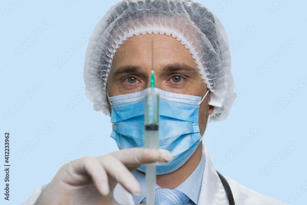 Close up portrait of mature male doctor pushing syringe. Isolated on blue background. Close up portrait of mature male doctor pushing syringe. Isolated on blue background.