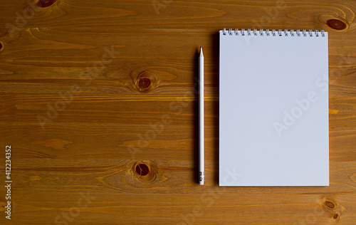 A white notebook and a white pencil on a wooden table.
