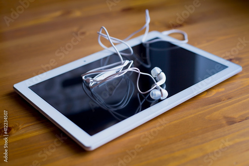 A white tablet and white headphones lie on a wooden table. Remote work from home.