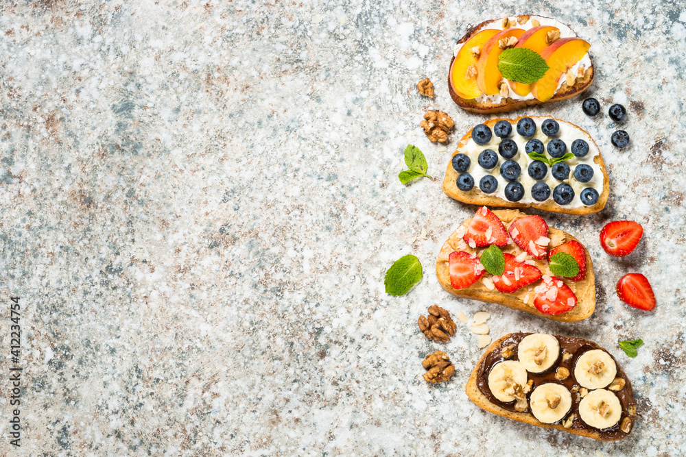 Sweet toast assortment. Chocolate banana, cream cheese and peach, peanut butter and strawberry, cream cheese and blueberry toasts. Stone background, top view. Sweet toast assortment. Chocolate banana, cream cheese and peach, peanut butter and strawberry, cream cheese and blueberry toasts. Stone background, top view.