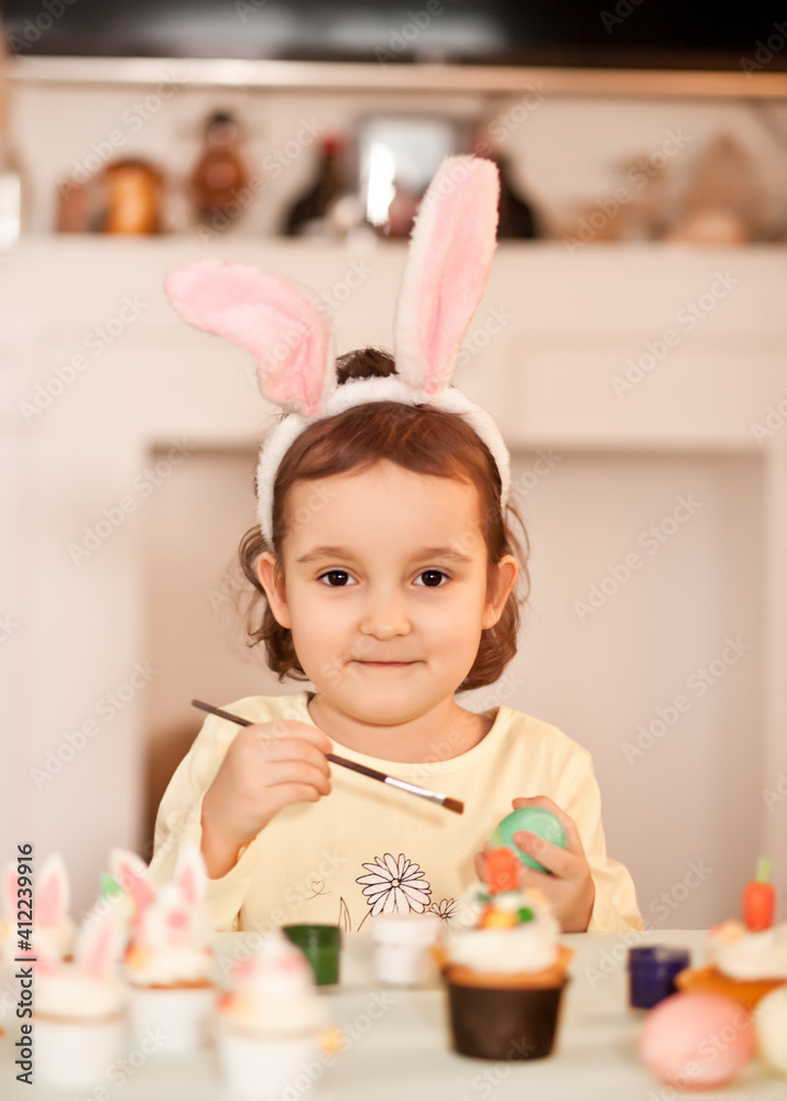 Funny girl child wearing bunny ears and painting Easter egg in spring time at home. Funny girl child wearing bunny ears and painting Easter egg in spring time at home.