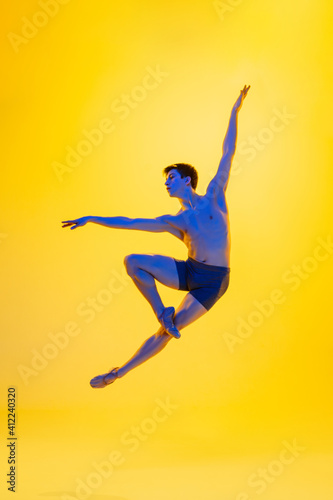 Inspiration. Young and graceful ballet dancer on yellow studio background in neon light. Art, motion, action, flexibility, inspiration concept. Flexible caucasian ballet dancer, moves in glow. © master1305