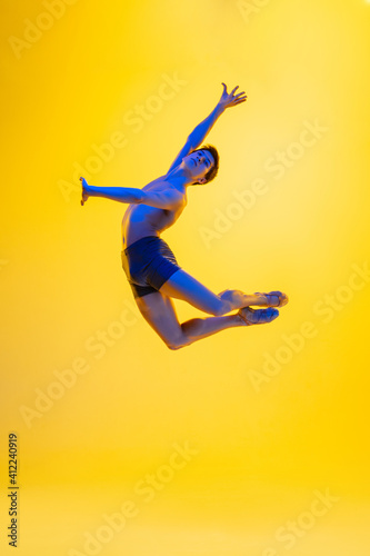 Artwork. Young and graceful ballet dancer on yellow studio background in neon light. Art, motion, action, flexibility, inspiration concept. Flexible caucasian ballet dancer, moves in glow. © master1305