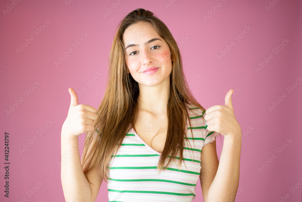 Smiling pretty young girl showing thumbs up isolated over pink background
