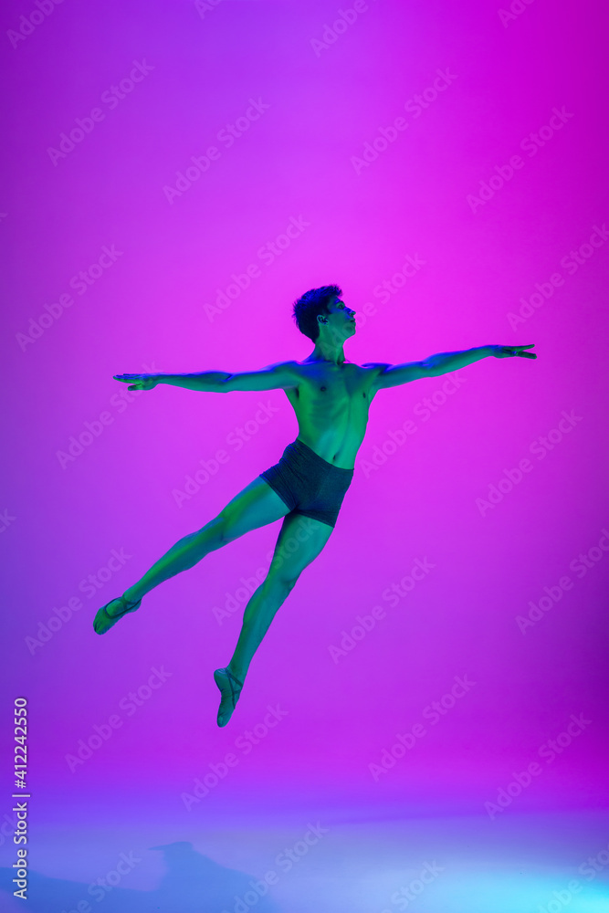 Flying. Young and graceful ballet dancer on purple studio background in neon light. Art, motion, action, flexibility, inspiration concept. Flexible caucasian ballet dancer, moves in glow.