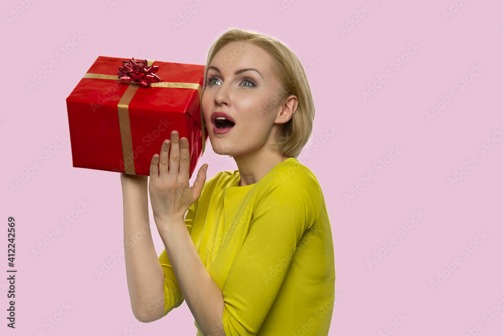 Curious surprised european lady with a gift box. Astonished adult woman isolated on pink background. Curious surprised european lady with a gift box. Astonished adult woman isolated on pink background.