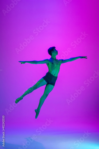 Flying. Young and graceful ballet dancer on purple studio background in neon light. Art  motion  action  flexibility  inspiration concept. Flexible caucasian ballet dancer  moves in glow.