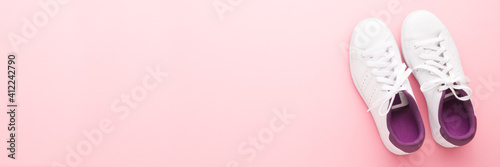 White female sport shoes for walking, running or fitness on light pink table background. Pastel color. Closeup. Wide banner. Empty place for text. Top down view.