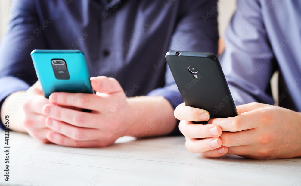 Two friends side by side use phones to type text messages - Hands and phone close up - Concept of modern technologies and content in social networks Two friends side by side use phones to type text messages - Hands and phone close up - Concept of modern technologies and content in social networks