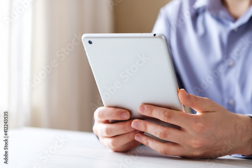 Tablet in the hands of a young man against the background of a blue shirt - Businessman uses a tablet to read and view content in social networks - Concept of modern technologies