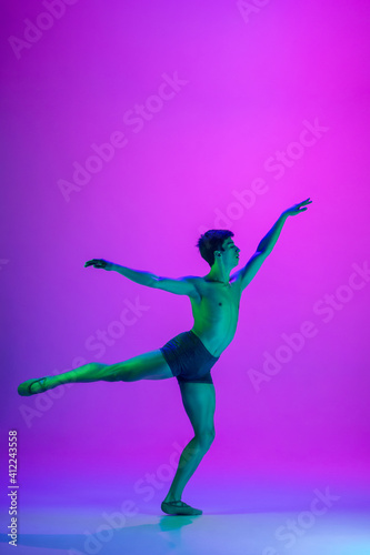 Feelings. Young and graceful ballet dancer on purple studio background in neon light. Art, motion, action, flexibility, inspiration concept. Flexible caucasian ballet dancer, moves in glow.