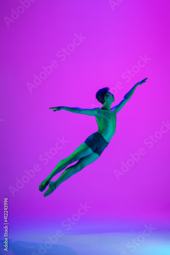 Feelings. Young and graceful ballet dancer on purple studio background in neon light. Art, motion, action, flexibility, inspiration concept. Flexible caucasian ballet dancer, moves in glow.