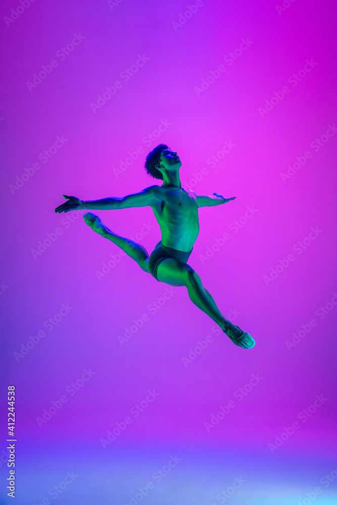 Weightless. Young and graceful ballet dancer on purple studio background in neon light. Art, motion, action, flexibility, inspiration concept. Flexible caucasian ballet dancer, moves in glow.