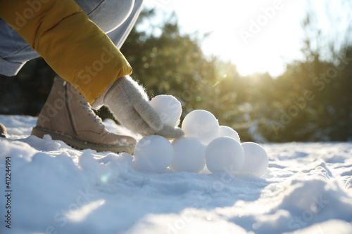 Woman rolling snowballs outdoors on winter day, closeup photo