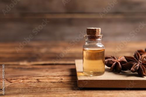 Bottle of essential oil and anise on wooden table. Space for text