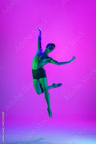 Emotions. Young and graceful ballet dancer on purple studio background in neon light. Art, motion, action, flexibility, inspiration concept. Flexible caucasian ballet dancer, moves in glow. © master1305