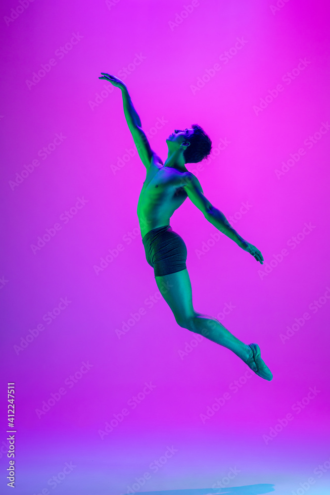 Weightless. Young and graceful ballet dancer on purple studio background in neon light. Art, motion, action, flexibility, inspiration concept. Flexible caucasian ballet dancer, moves in glow. Weightless. Young and graceful ballet dancer on purple studio background in neon light. Art, motion, action, flexibility, inspiration concept. Flexible caucasian ballet dancer, moves in glow.