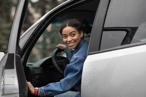 Friendly smiling millennial african american female driver opens door and looks for fellow traveler © Prostock-studio
