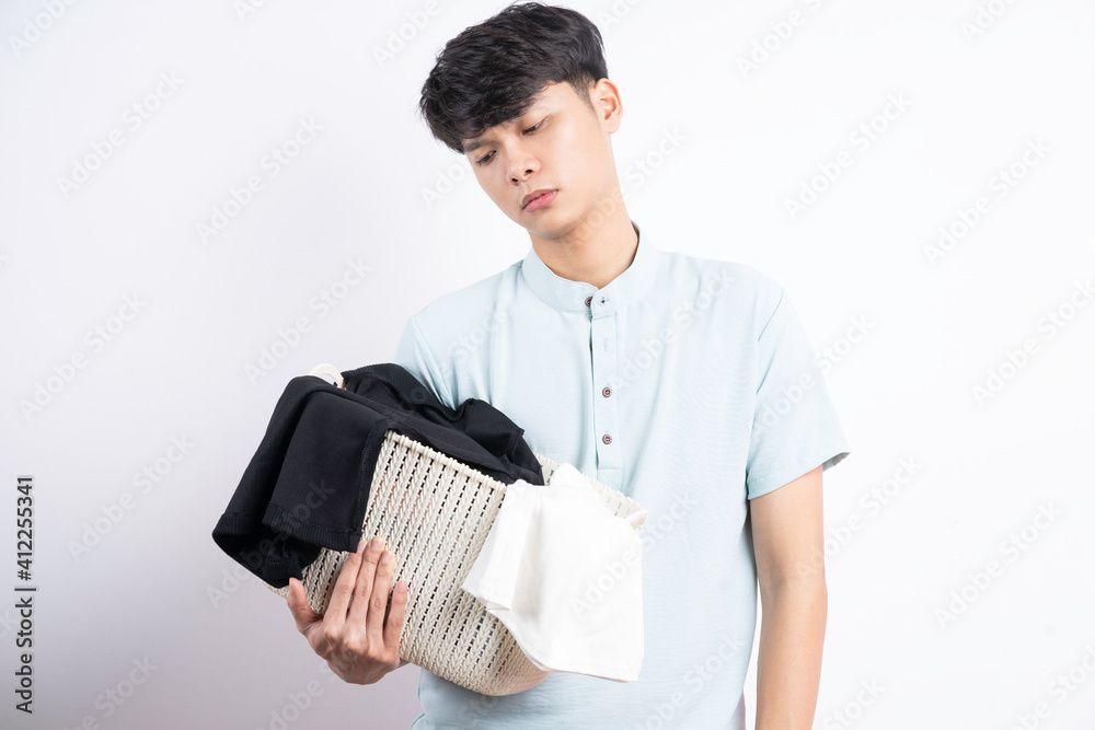 Young Asian man holding basket of clothes with gestures on white background Young Asian man holding basket of clothes with gestures on white background