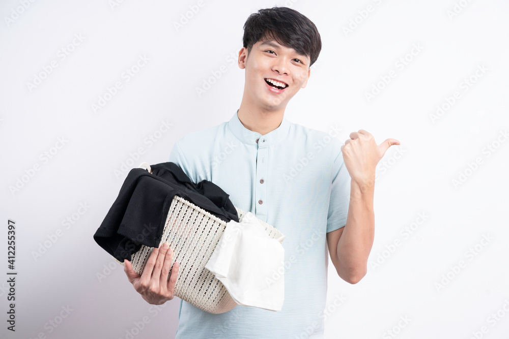 Young Asian man holding basket of clothes with gestures on white background Young Asian man holding basket of clothes with gestures on white background