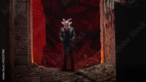 Devil looking at the camera. Mysterious masked man in a ruined mansion. Hallway with red lights, scary person in a haunted house. Nightmare about demon in hell.