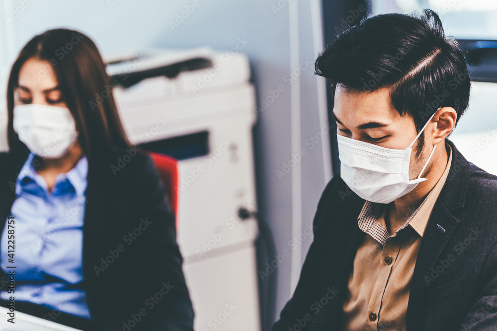 Asian employee woman in face mask watching colleague working at desk. new normal people adaptation in office. business company reopen concept