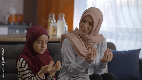 Muslim little girl in hijab and with her Muslim mother pray at home.Muslim mother and daughter pray together at home and then hug. Prayer concept.