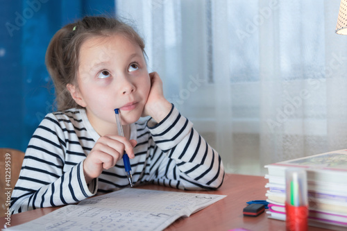 Dreamy little girl sit at desk studying look in distance visualizing or thinking, small child dreamer feel unmotivated distracted from preparing doing homework at home, lost in dreams or imagination