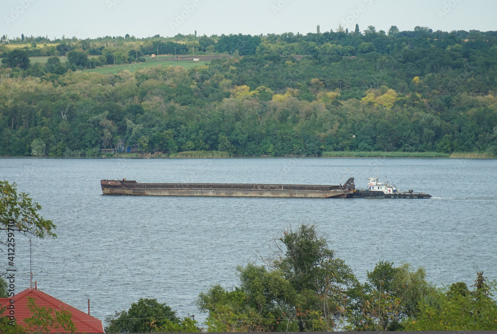 A barge cargo ship is sailing along the river.     