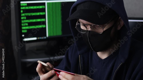 male hacker in a mask and a cap is engaged in cybercrime, stealing money from payment cards.