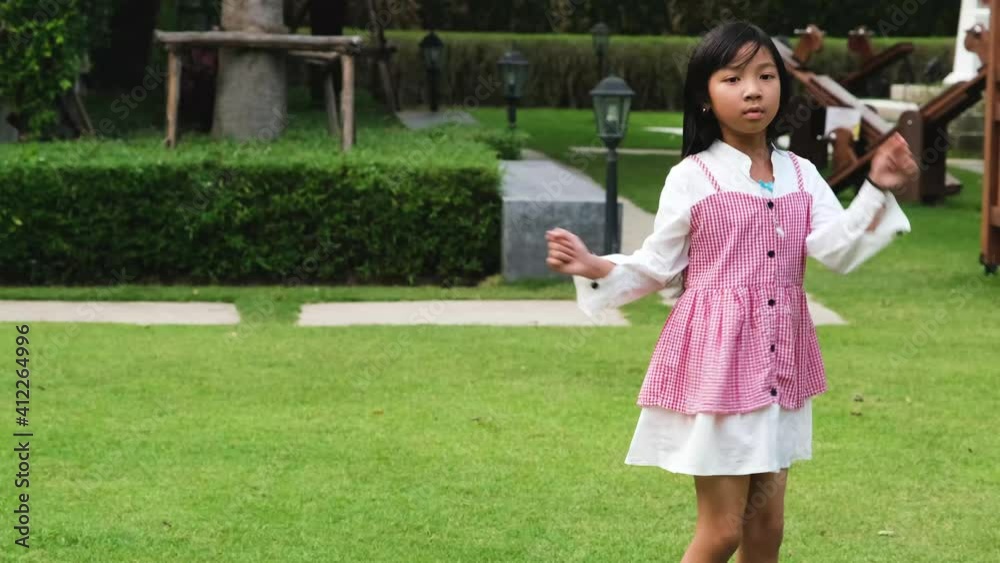 Asian child girl wears a red and white shirt dancing in the courtyard in a good mood Asian child girl wears a red and white shirt dancing in the courtyard in a good mood