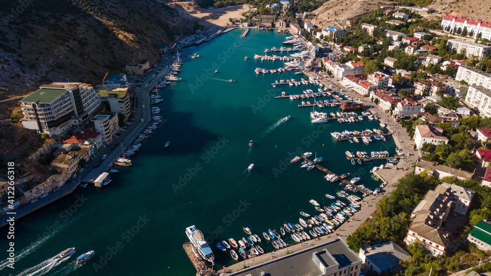 Aerial view of the bay with a lot of white boats and yachts at sunset on sunny day. View from above of pier for pleasure boat and sailboats in marina with beautiful turquoise sea.