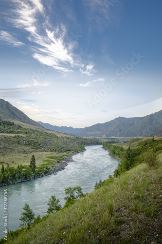 Landscape with a river, green banks, mountains and blue sky. Altai Republic, Kur-Kechu cordon on the Katun River. The beauty of nature, relaxation in the mountains, escape from civilization concept.