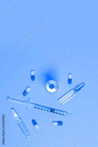 Medical syringe with liquid and tablets and pills on pink background. Cosmetology or vaccination concept. Flat lay, copy space.