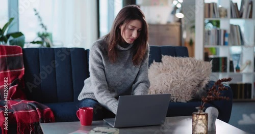 Young beautriful caucasian woman working on freelancer project at home. Relaxed casual girl using laptop in stylish lliving room interior. photo