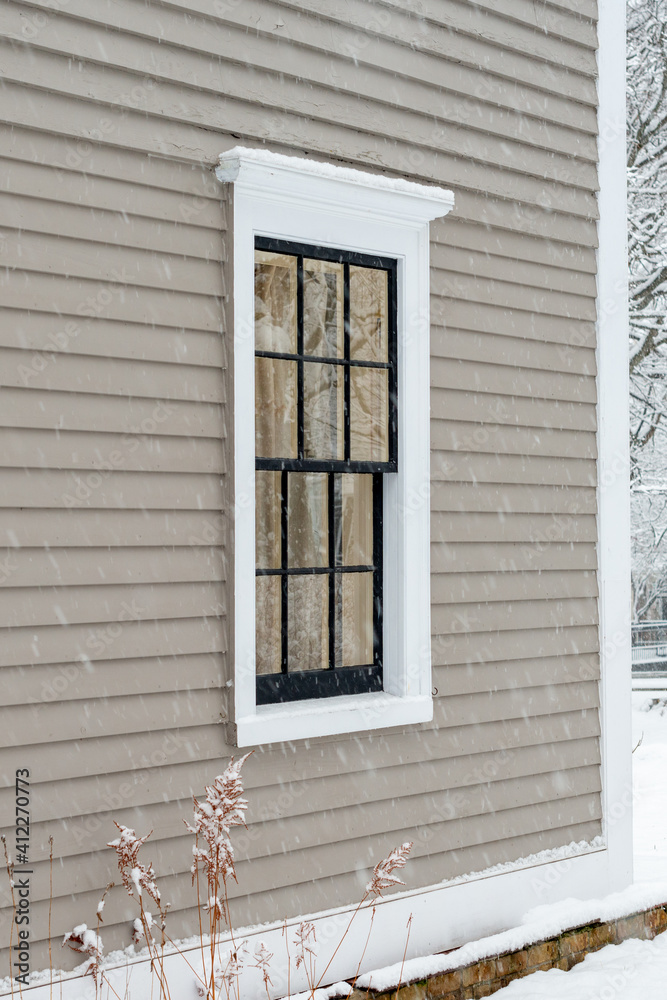 A vintage double hung window with reflecting glass on a beige colour exterior wall of a building. The window has a dark green with white trim. There's a rock foundation below the wood clapboard wall.
