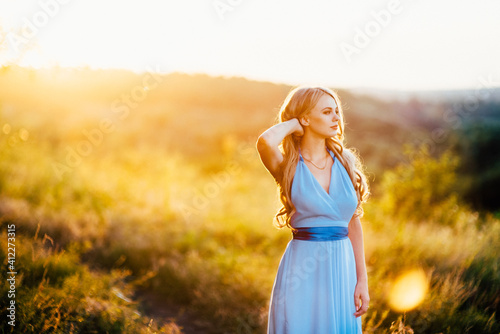 blonde with loose hair in a light blue dress in the light of sunset