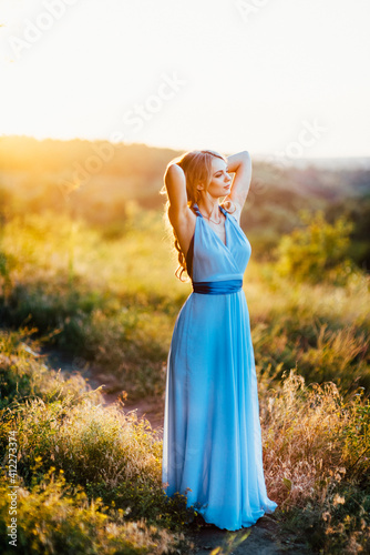 blonde with loose hair in a light blue dress in the light of sunset