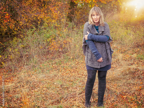 A woman of 40 years in autumn nature landscape. The blonde woman wears clothes made of wool and boots.