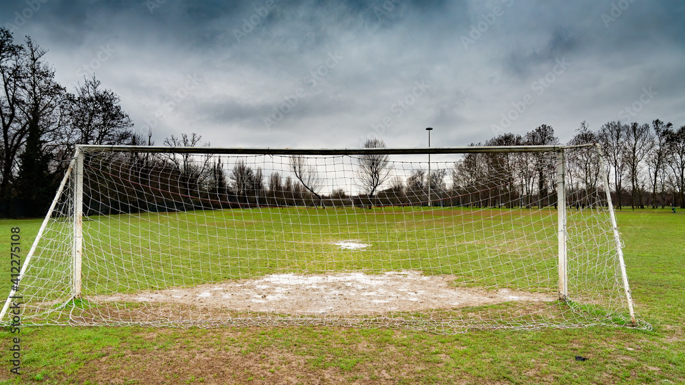 Fototapeta premium Goal post from behind in an abandoned soccer field. Dramatic stormy sky on the horizon.