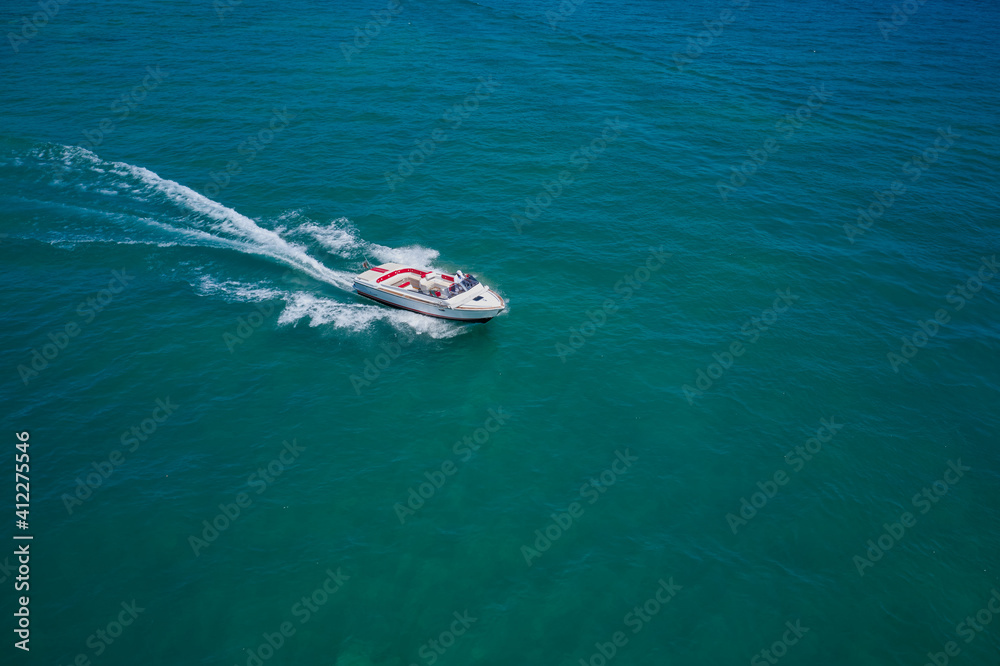 Drone view of a boat sailing. Top view of a white boat sailing to the blue sea. Motor boat in the sea. Travel - image. Drone view of a boat sailing. Top view of a white boat sailing to the blue sea. Motor boat in the sea. Travel - image.