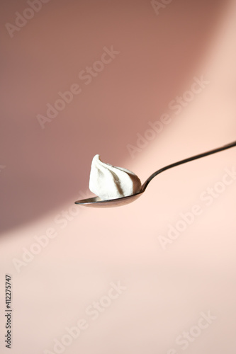Sweet tasty meringue or marshmallow in tea spoon on pastel pink background with shadows. Minimalism food concept.