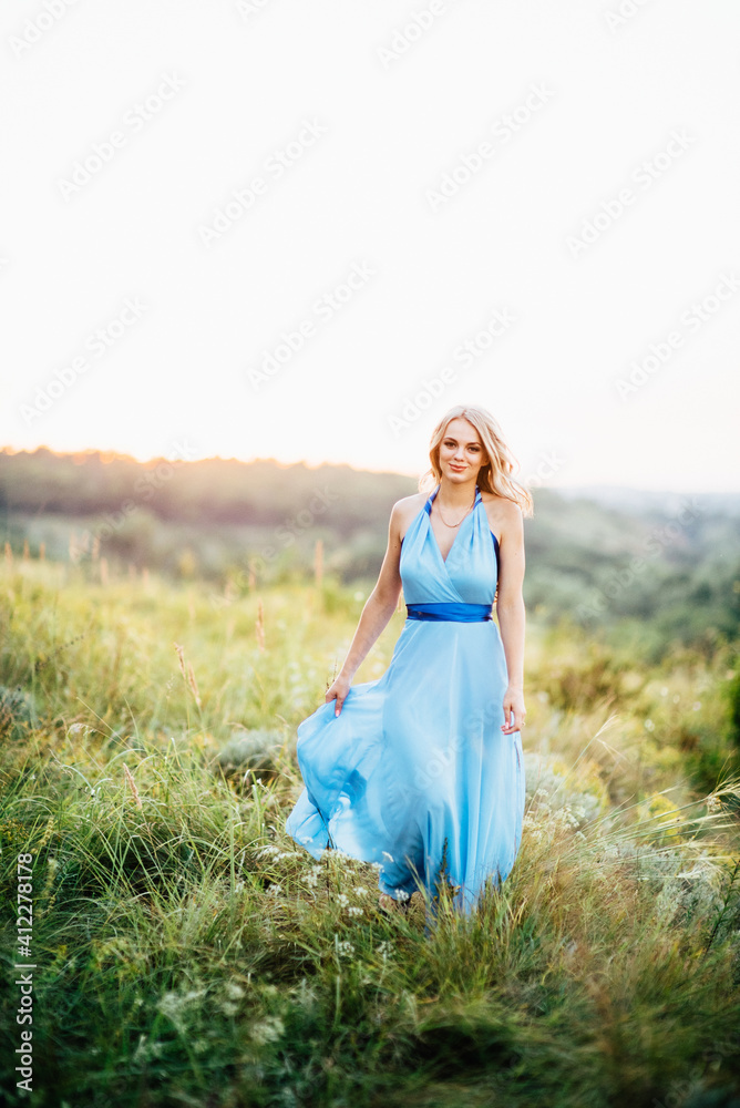Obraz premium blonde girl with loose hair in a light blue dress and a guy in the light of sunset