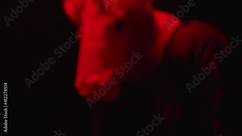 Close up of a tortured man in mask. Dark interrogation scene, terrorist questioned. Creepy horror scene, red flashing lights in the dungeon. Man in pain.