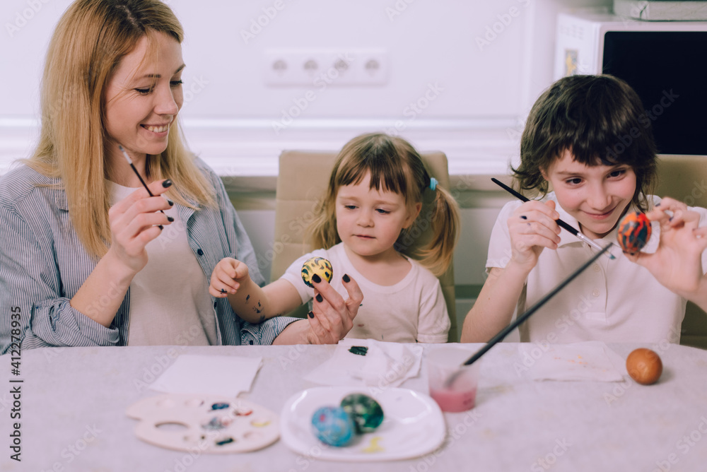 Preparing for Easter. The family is painting Easter eggs at home in the kitchen. Mom teaches her daughters to draw. Medium shot. Preparing for Easter. The family is painting Easter eggs at home in the kitchen. Mom teaches her daughters to draw. Medium shot.