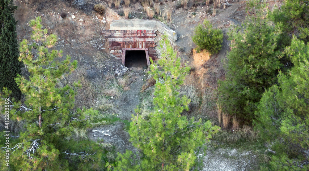 Open entrance into old abandoned mine hidden behind the trees, aerial view