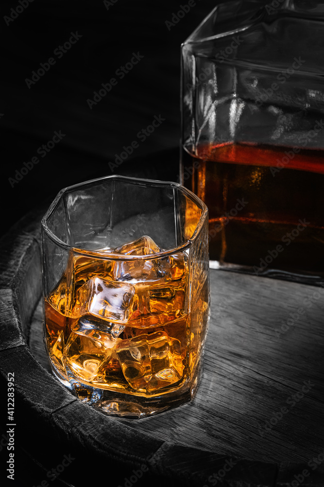 Barrel of scotch whiskey with a decanter of whiskey and glass of whiskey with ice on a black background. Bottle and glass of whiskey with ice on a wooden background