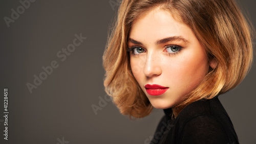 Closeup portrait of an young adult girl with medium length hair. Photo of a fashion model posing at studio. Pretty young woman with red lips looking at camera. Beauty portrait.